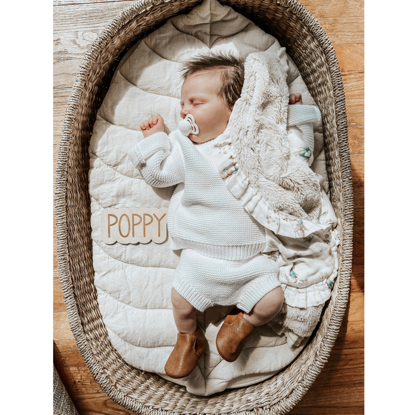 Photo of a newborn laying in a basket with a personalized name sign that says Poppy