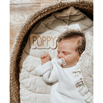 Photo of a newborn laying in a basket with a personalized name sign that says Poppy